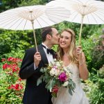 Bride and groom holding parasols while groom kisses bride on cheek