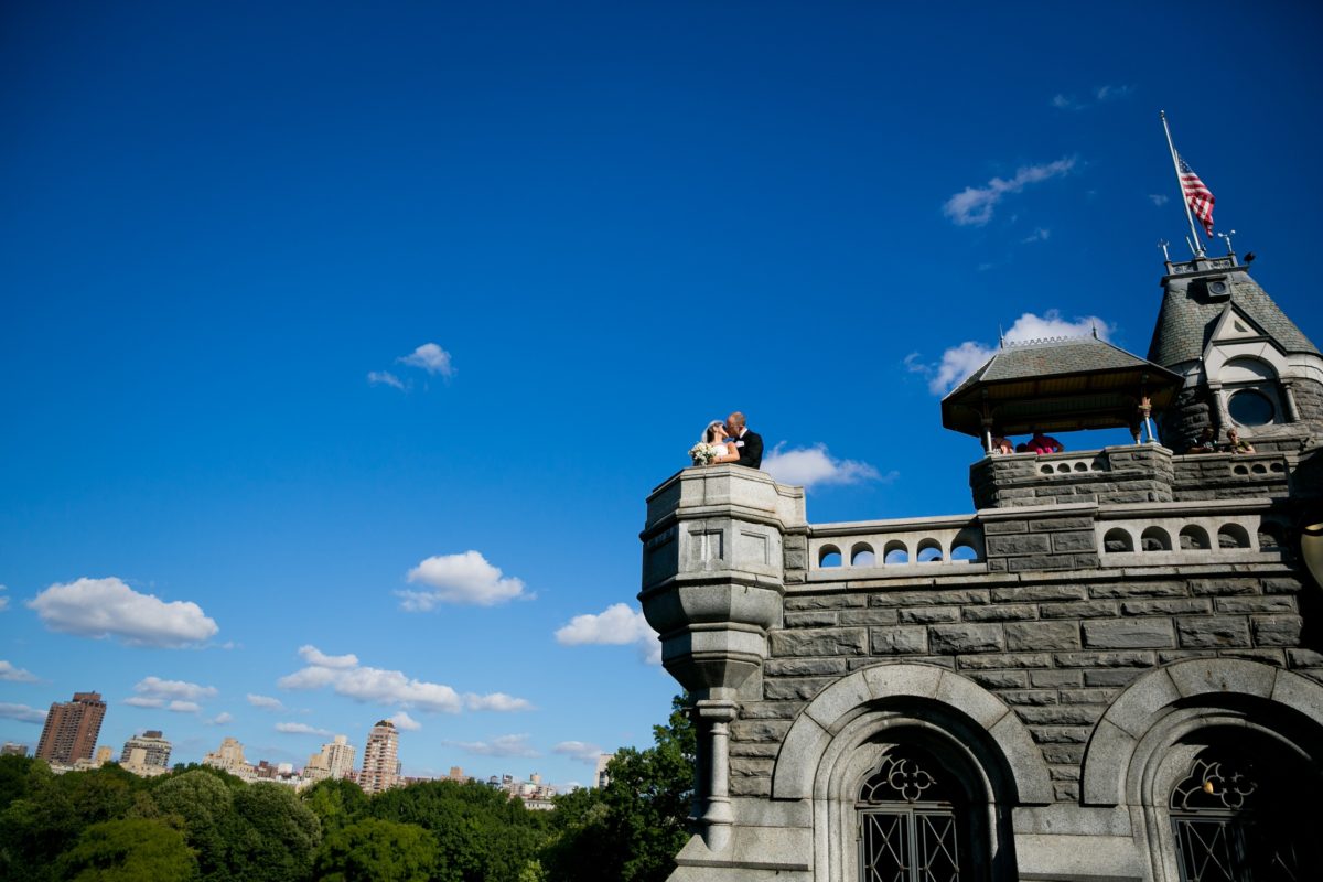 Bride and groom kiss on top of Belvedere Castle against a blue sky