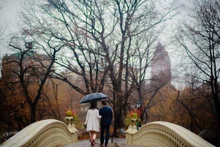 Newlyweds walk away on Bow Bridge holding umbrella