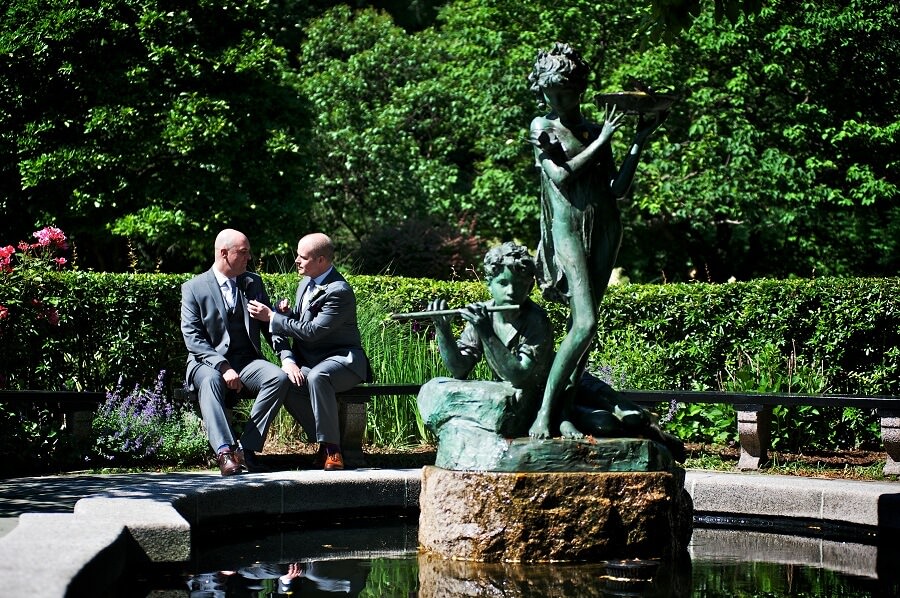 Gay couple poses by fountain in South Garden on sunny day