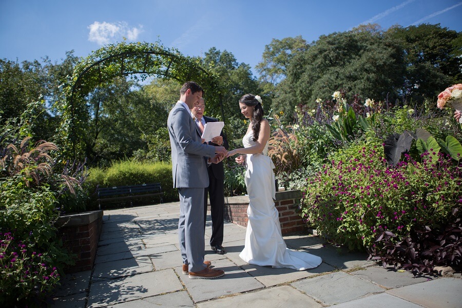 Couple exchanges ring in front of archway in North Garden in Central Park