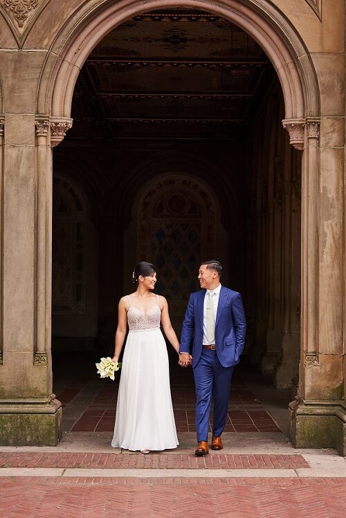 Wedding couple walks walks through arches at Bethesda Fountain