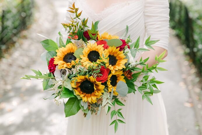 Garden style bridal bouquet of sunflowers and greenery with red rose accents